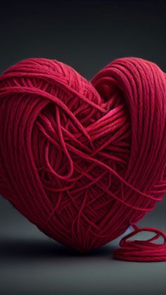 a ball of yarn in the shape of a heart on a dark background with a red thread