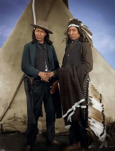 two native american men standing next to each other in front of a teepee tent