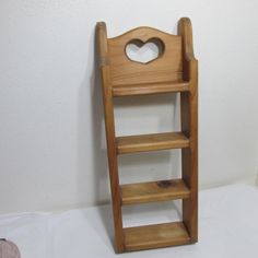 a wooden chair with a heart shaped hole in the back and shelf below it, against a white wall