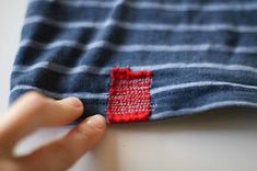 someone is stitching something on top of a blue and white striped shirt with red trim