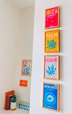 four framed art pieces on the wall above a shelf in a room with white walls