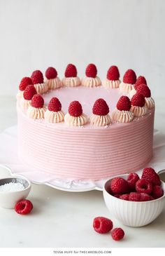 a pink cake with white frosting and raspberries on top