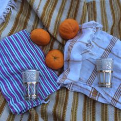 three oranges and two silver shot glasses on a striped cloth with an old towel