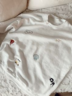 a white shirt with embroidered patches on it sitting on a bed next to a pillow