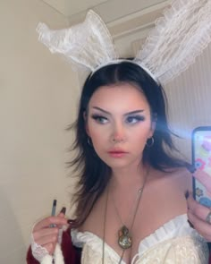 a woman with bunny ears holding up a cell phone in her hand and looking at the camera