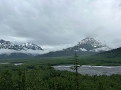 the mountains are covered in snow and clouds as they sit on top of some trees