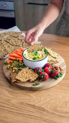 a person dipping some crackers into a bowl of dip surrounded by fruit and veggies