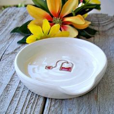 a white bowl sitting on top of a wooden table next to yellow and red flowers