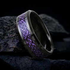 a purple ring with an intricate design on it sitting on top of a rock in the dark