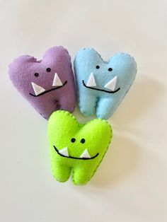 three stuffed animals with mouths and teeth are on a white surface in the shape of hearts