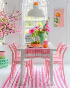 a dining room table with pink chairs and flowers