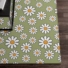 a book is laying on top of a green flowered tablecloth with white daisies