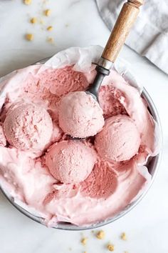 a bowl filled with pink ice cream on top of a white counter next to a wooden spoon