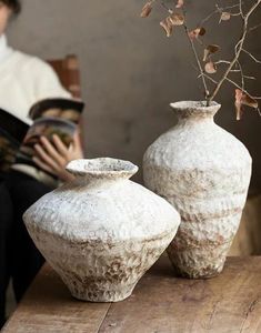 two white vases sitting on top of a wooden table next to each other with branches in them