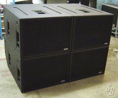 two large black speakers sitting on top of each other in a room with equipment behind them