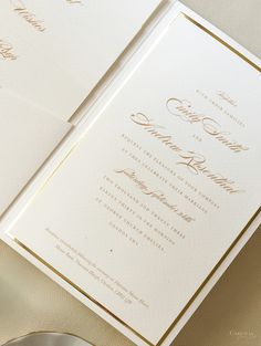 two white and gold wedding cards on top of a table with a silver plate next to it