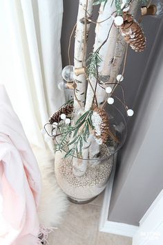 a vase filled with pine cones and other decorations on top of a floor next to a window