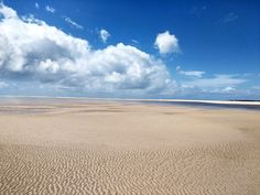 a sandy beach with waves coming in to the shore and clouds above it on a sunny day