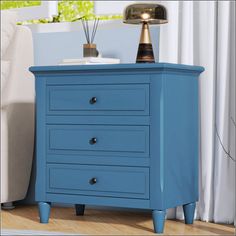 a blue chest of drawers with two lamps on top and a white couch in the background