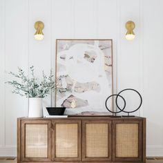 an art piece on top of a wooden cabinet in front of a painting and plant