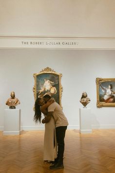 two people hugging each other in an art gallery with paintings on the wall behind them