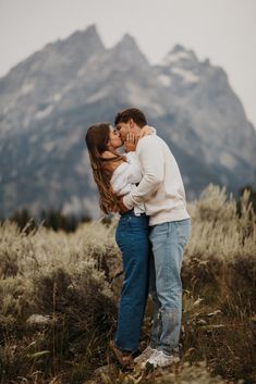 a man and woman kissing in front of a mountain