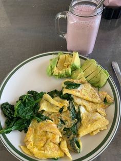 an omelet with spinach and avocado on a plate next to a glass of milk