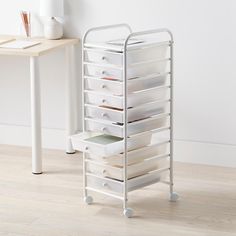 a white cart with lots of drawers on top of it next to a wooden table