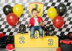 a young boy sitting on top of a yellow podium in front of red and black balloons