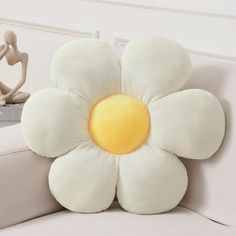 a flower shaped pillow sitting on top of a couch next to a figurine