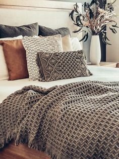 a bed covered in pillows and blankets next to a vase with flowers on the headboard