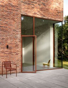 an empty chair sitting in front of a brick building with glass doors on the outside