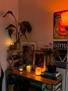 a table with books and candles on it in a room filled with pictures, plants and other things