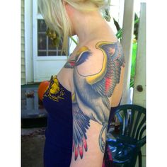 a woman with a bird tattoo on her arm and shoulder is standing in front of a house