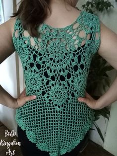 a woman wearing a green crochet top with her hands on her hips, standing in front of a plant