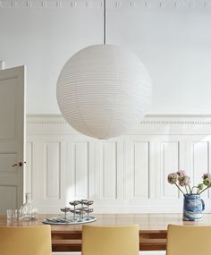 a dining room table with yellow chairs and a white ball hanging from the ceiling over it