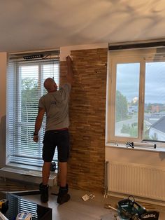 a man is working on a brick wall in his living room with the window open