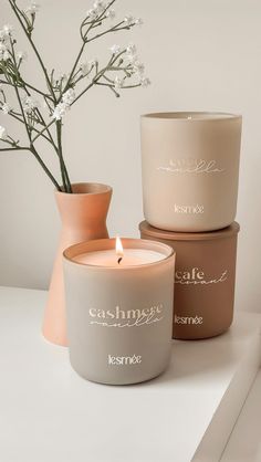 three candles sitting next to each other on top of a white table with flowers in vases