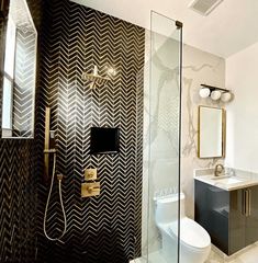 a bathroom with black and white wallpaper, gold accents and a glass shower door