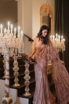 a woman in a pink sari is standing on the stairs with candles behind her