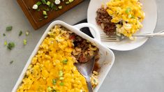 two white dishes filled with macaroni and cheese on top of a wooden cutting board