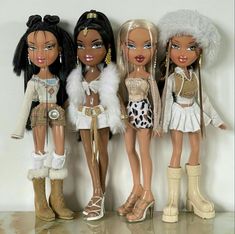 four dolls are standing next to each other in front of a white wall and one has her hair pulled back