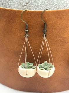 two white ceramic pots with green plants hanging from hooks on a brown leather potted planter