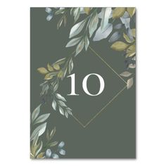 the table number is surrounded by green leaves and gold accents on a gray background with a white diamond in the center