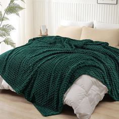 a large green blanket sitting on top of a bed next to pillows and pillow cases