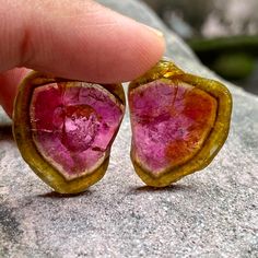 a pair of pink and yellow heart shaped earrings sitting on top of a gray rock