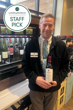 a man holding a bottle of wine in front of a display case with bottles of wine