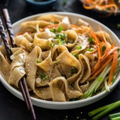 a white bowl filled with noodles and veggies next to some chopsticks