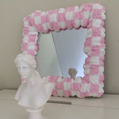 a pink and white sculpture sitting next to a mirror on top of a dresser under a light