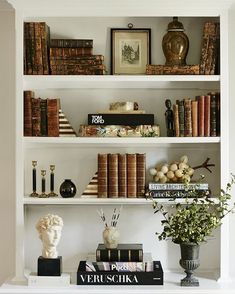 a white book shelf filled with books and vases on top of it's shelves